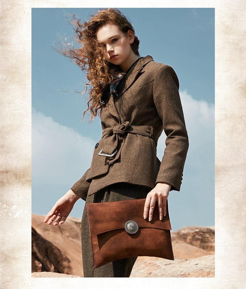 Woman holding large handcrafted brown leather clutch bag with decorative clasp outdoors
