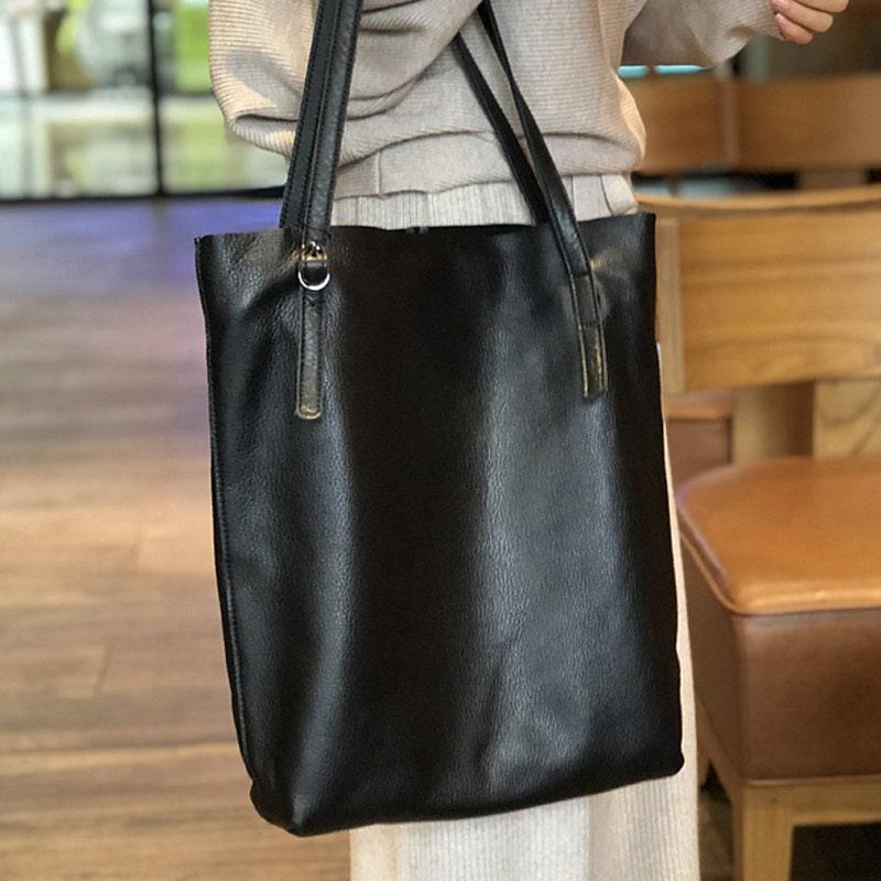 Large black leather tote bag with shoulder straps, shown in a casual indoor setting