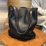 Large black leather tote bag with double handles on a wooden table, modern minimalist design