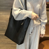 Woman carrying large black leather tote bag on shoulder, casual indoor setting