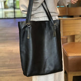Oversized black leather tote bag with double handles, carried indoors