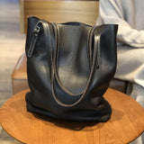 Oversized black leather tote bag with double handles on a wooden table indoors