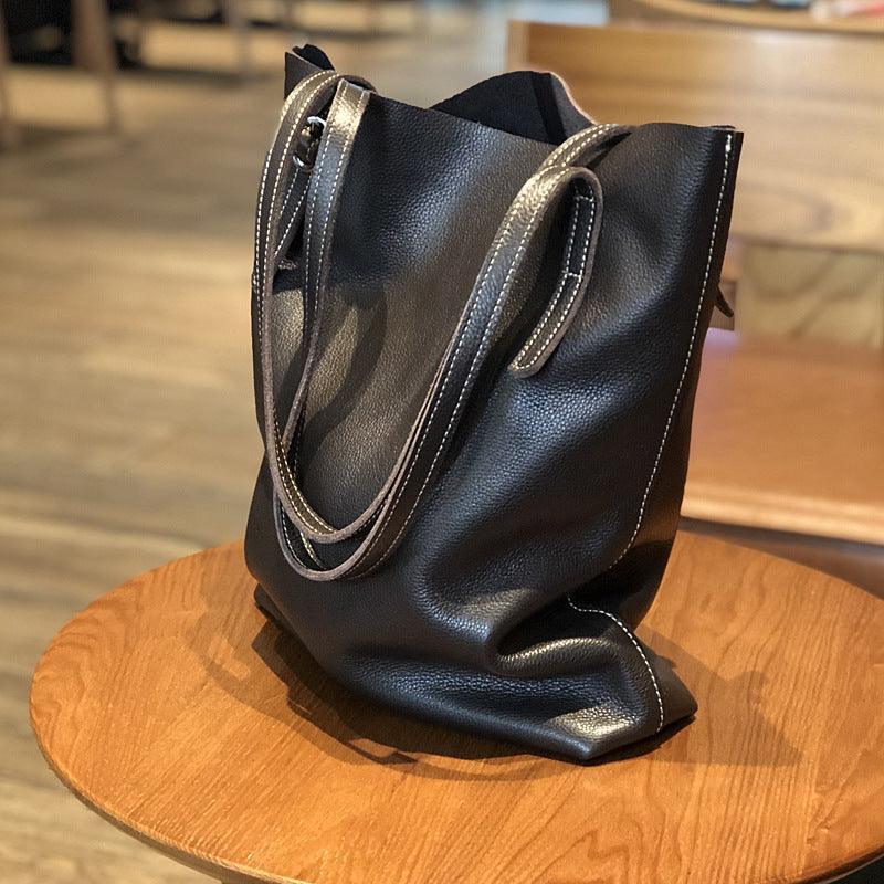 Oversized black leather tote bag with dual handles and contrast stitching on a wooden chair