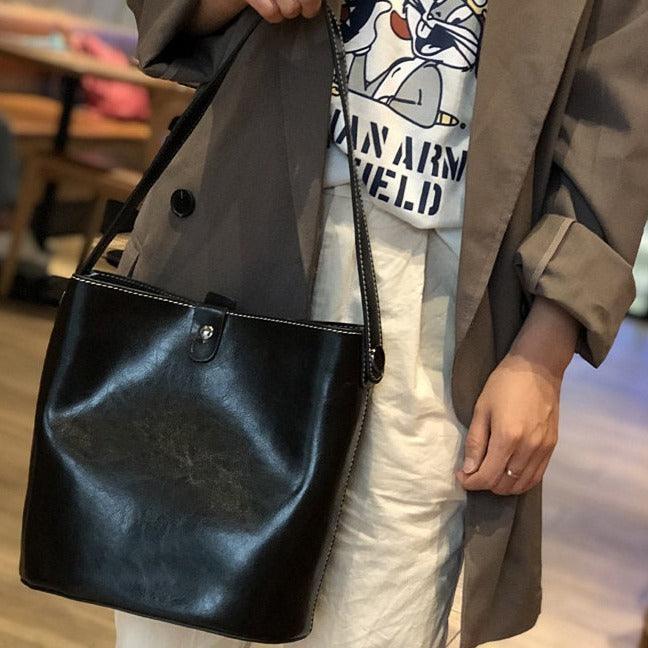 Black leather bucket bag with shoulder strap worn crossbody by person in casual outfit