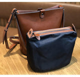 Brown leather bucket bag with detachable black zip pouch on wooden table