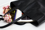Large black full grain leather tote bag with magazines and pink flowers inside