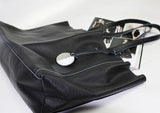 Black full grain leather tote bag with long handles and round metal charm on white background