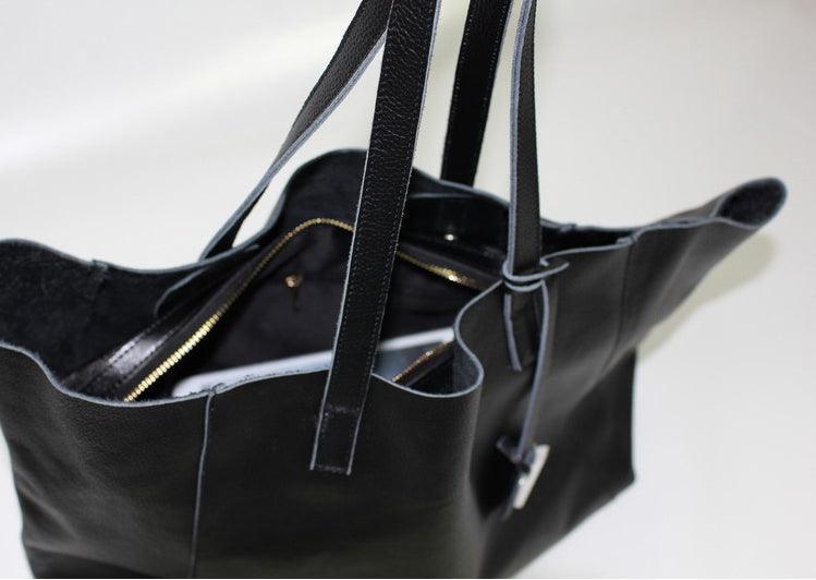 Black full grain leather tote bag with zipper pocket and double straps on white background