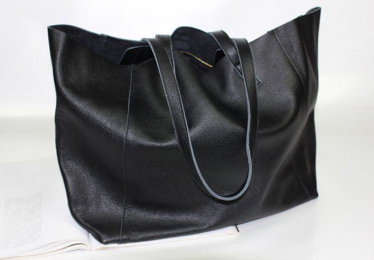 Black full grain leather tote bag with dual handles, minimalist design, on a white surface