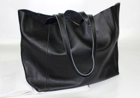 Black full grain leather tote bag with dual handles, minimalist design, on a white surface