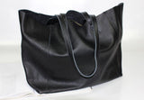 Black full grain leather tote bag with dual handles, minimalist design, on a white surface