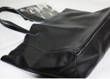 Black full-grain leather tote bag with double handles on a light background