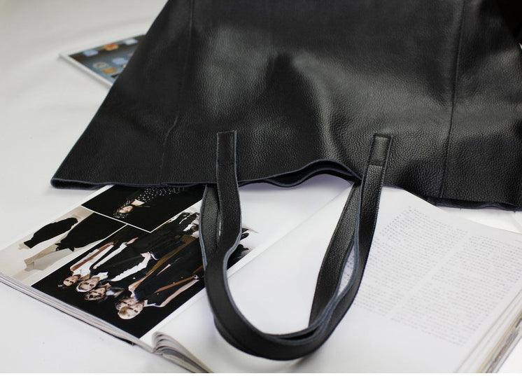 Black full grain leather tote bag with dual handles on open magazine pages
