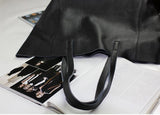Black full grain leather tote bag with dual handles on open magazine pages