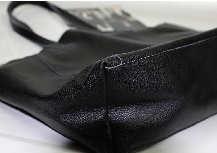 Black full grain leather tote bag with sturdy handles and visible stitching on a white surface