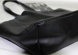 Black full grain leather tote bag with sturdy handles and visible stitching on a white surface