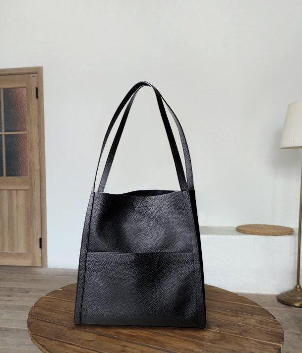 Black grain cowhide leather tote bag with shoulder straps on wooden table, minimalist design