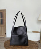 Black grain cowhide leather tote bag with shoulder straps on wooden table, minimalist design