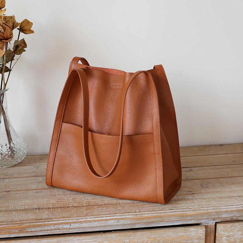 Minimalist grain cowhide leather tote bag with shoulder straps on wooden surface