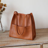Minimalist grain cowhide leather tote bag with shoulder straps on wooden surface