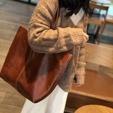 Woman wearing a large brown minimalist leather tote bag on shoulder indoors