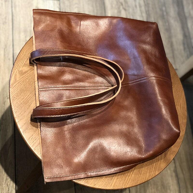 Minimalist large brown leather tote bag with double handles on a wooden table