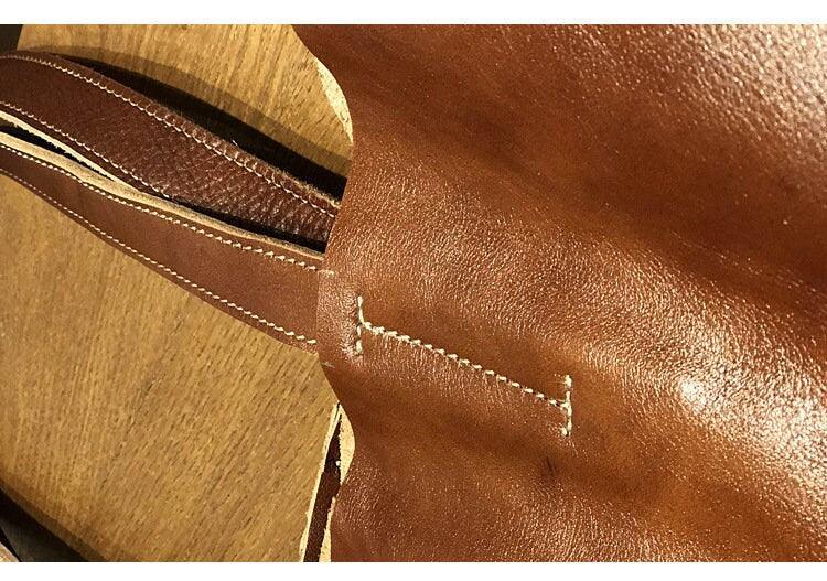 Close-up of brown minimalist leather tote bag handle and stitching detail on wooden surface