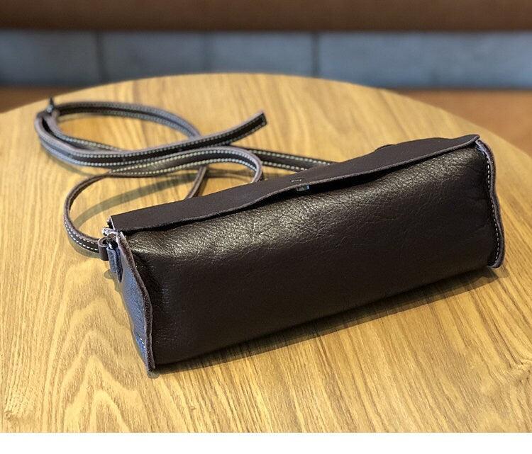 Minimalist small black leather crossbody bag with long strap on wooden table