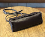 Minimalist small black leather crossbody bag with long strap on wooden table