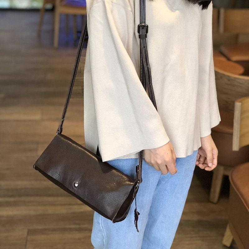 Minimalist black leather crossbody bag with shoulder strap on woman wearing casual outfit