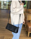 Minimalist small black leather crossbody bag with long strap worn over shoulder