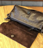 Small brown leather crossbody bag with suede interior and magnetic snap closure on table