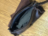 Open small black leather crossbody bag with zipper, interior pocket, on wooden surface