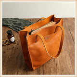 Natural cowhide leather tote handbag with zipper, shoulder straps, on wooden surface