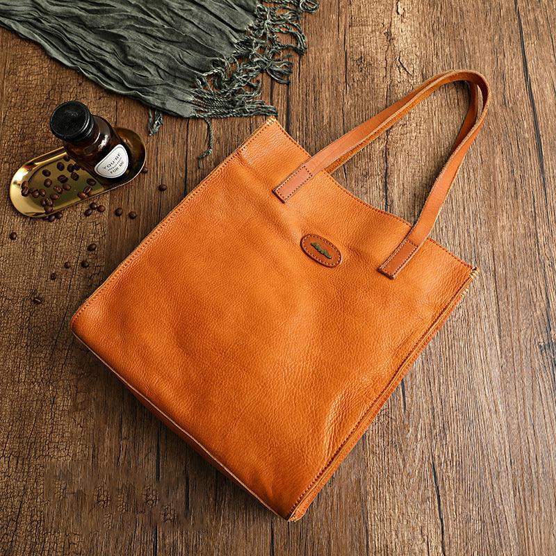 Natural tan cowhide leather tote handbag with shoulder straps on rustic wooden surface