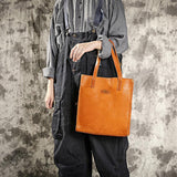 Woman holding a natural tan cowhide leather tote handbag with shoulder straps