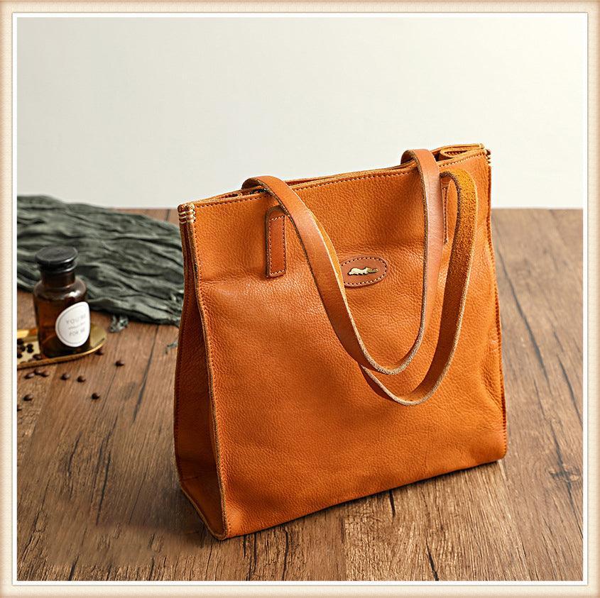 Natural tan cowhide leather tote handbag with double shoulder straps on wooden table