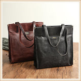 Brown and black cowhide leather tote handbags with shoulder straps on a wooden table