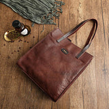 Brown cowhide leather tote handbag with shoulder straps on wooden surface