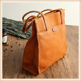 Natural tan cowhide leather handbag tote with shoulder straps on wooden table
