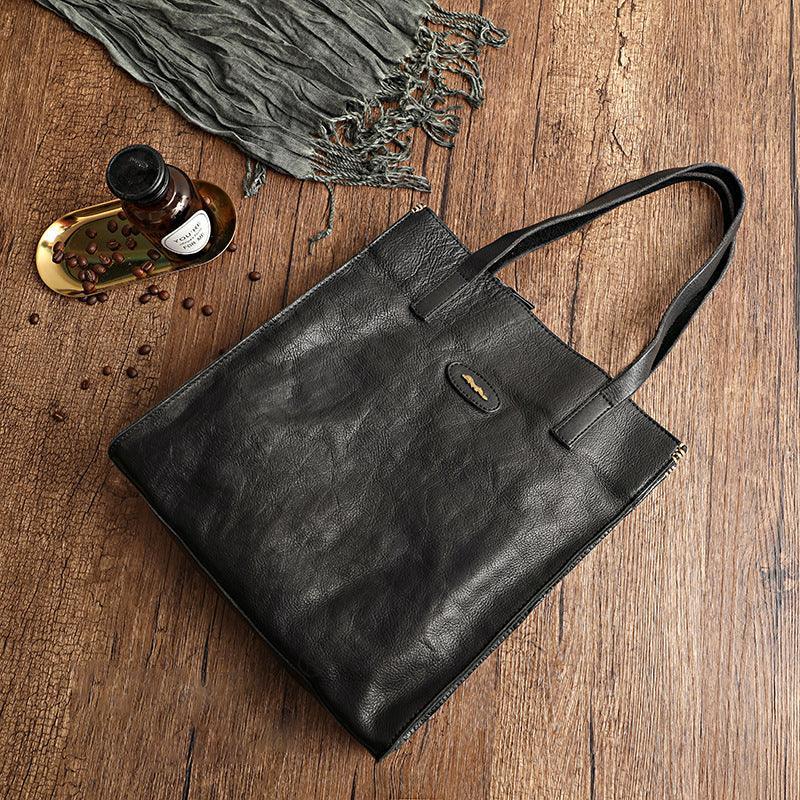Black cowhide leather handbag tote with shoulder straps on wooden surface, rustic setup
