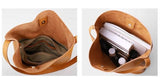 Interior view of tan cowhide leather tote bag with suede lining, zip pocket, and spacious compartments holding books and accessories.