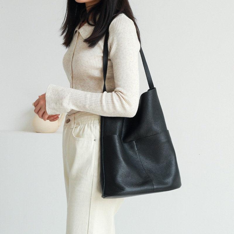 Woman wearing a black cowhide leather tote bag with front pockets and minimalist design