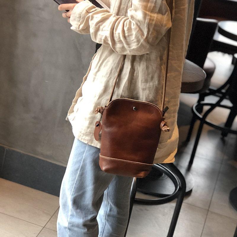 Small genuine leather crossbody shoulder bag in brown with retro design, worn by person indoors