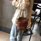 Small genuine leather crossbody shoulder bag in brown with retro design, worn by person indoors