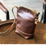 Small genuine leather crossbody bag with tan stitching on a wooden table