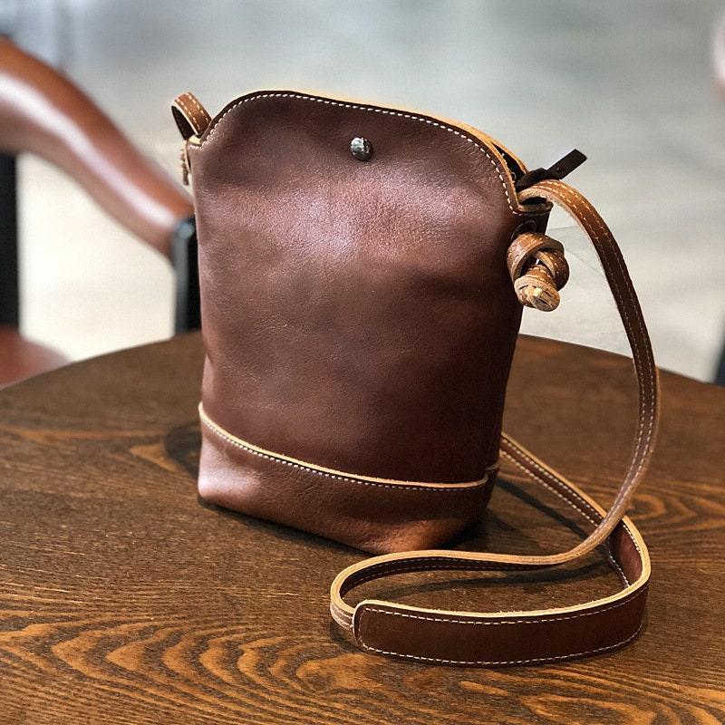 Small brown genuine leather crossbody shoulder bag with retro stitching on wooden table