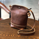 Small brown genuine leather crossbody shoulder bag with retro stitching on wooden table