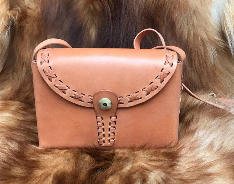 Small handcrafted leather shoulder bag with stitched flap and brass button, on fur background