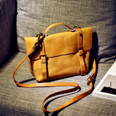 Vintage cowhide leather messenger bag with adjustable strap on grey couch